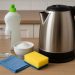 Electric kettle being cleaned with vinegar and sponge on a kitchen countertop